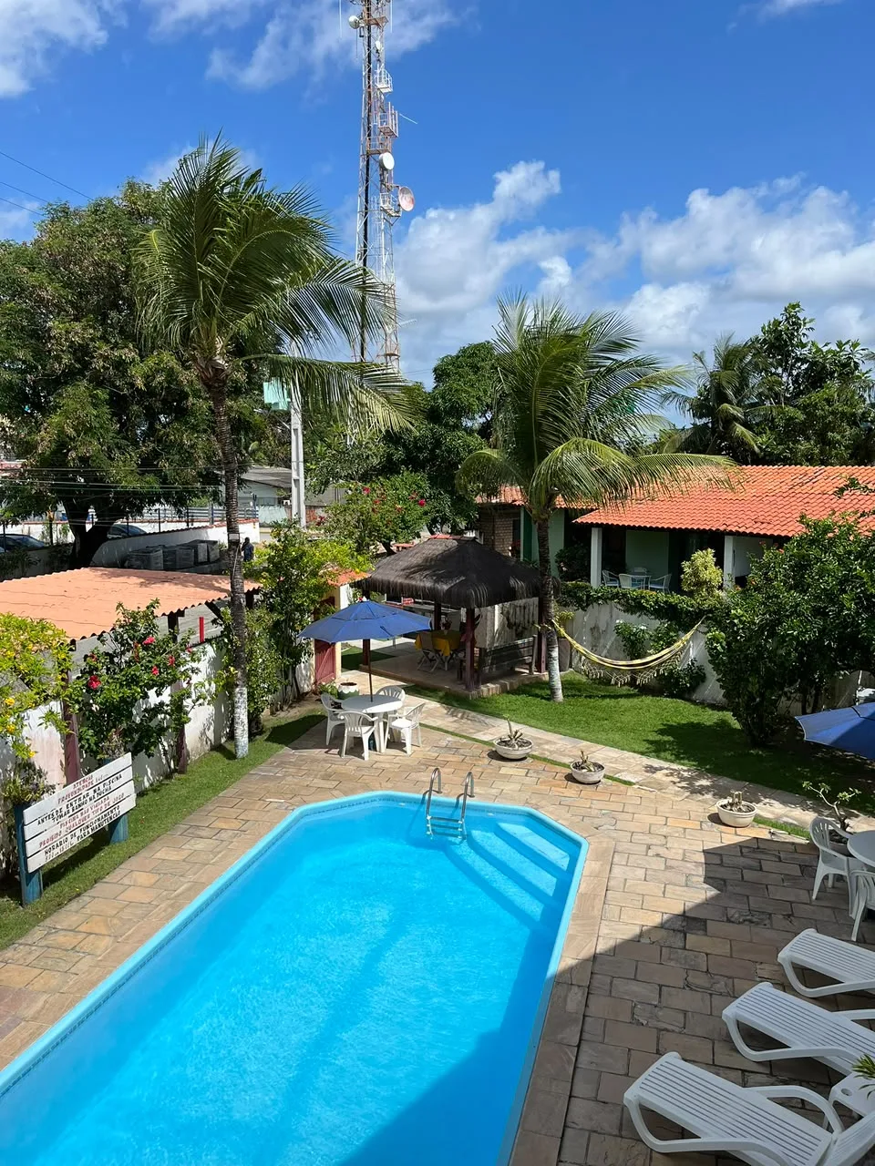 Vista do alto da piscina, do jardim com rede e do quiosque de palha