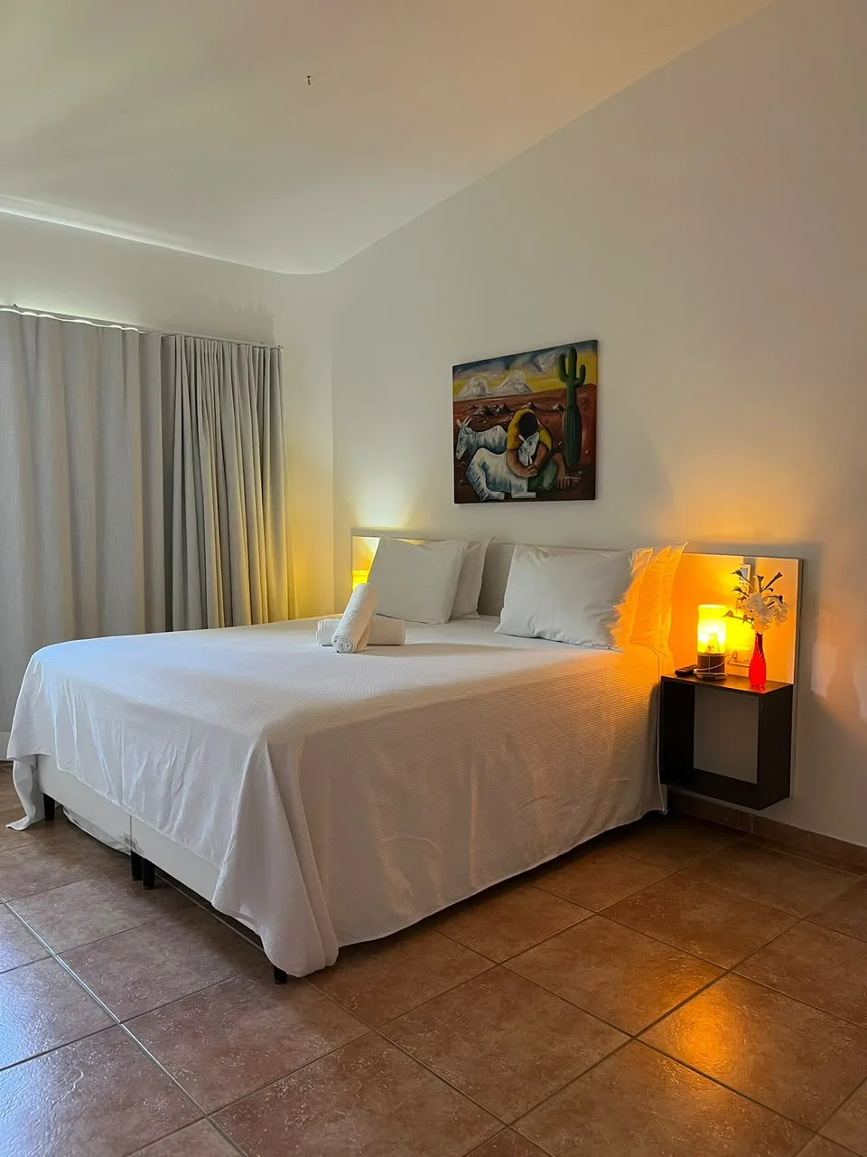 Quarto com cama king, luminárias acesas e quadro colorido na parede