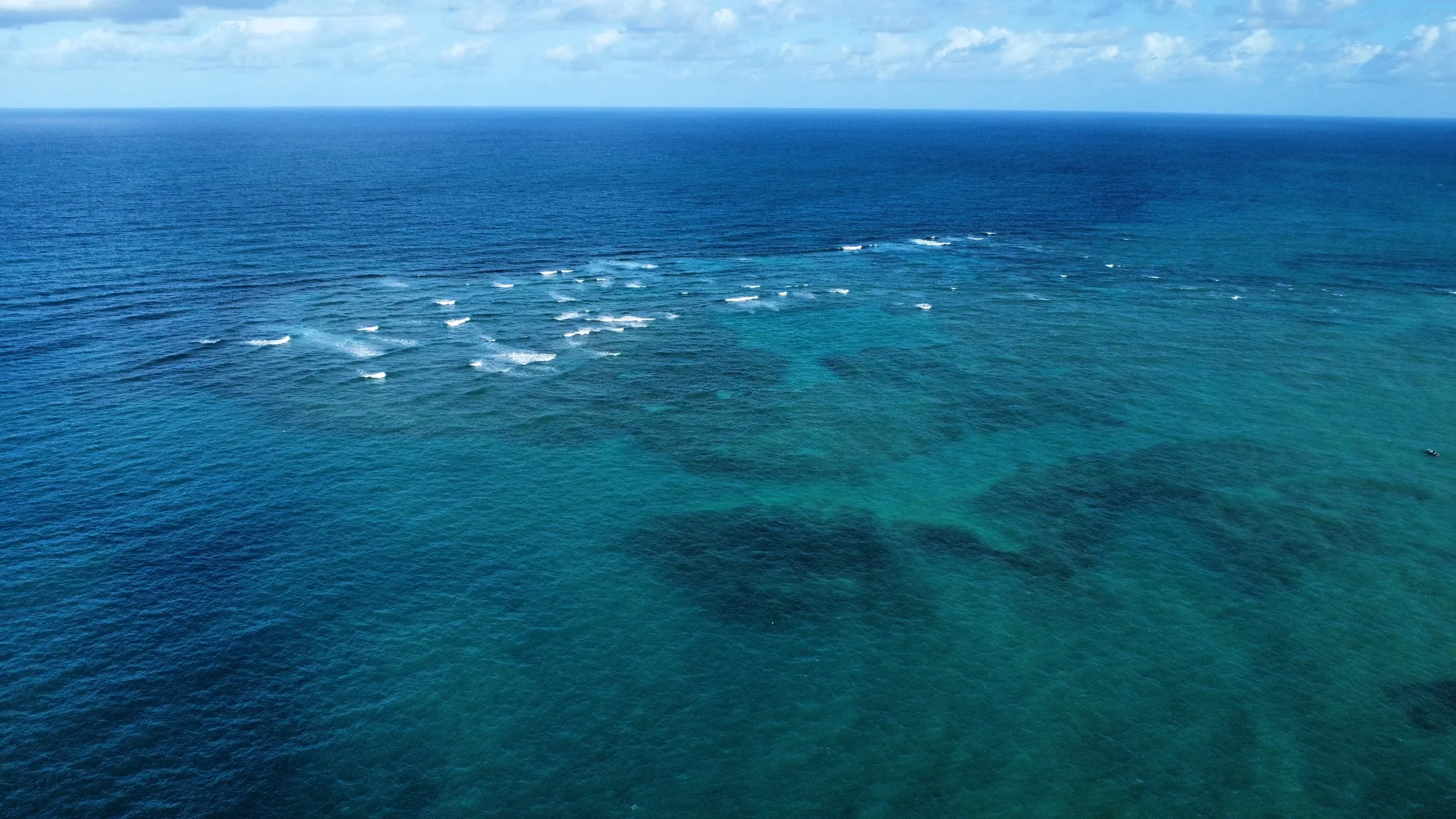 Recifes vistos do alto, no limite entre o azul profundo do mar aberto e o turquesa das piscinas naturais