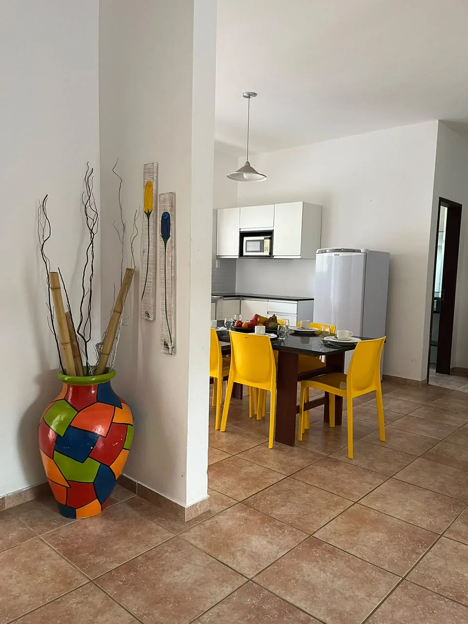 Sala com mesa de jantar de cadeiras amarelas e cozinha equipada