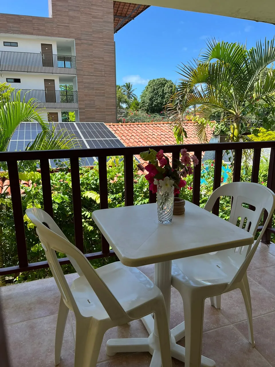Varanda de apartamento com mesa, cadeiras e coqueiros ao redor